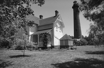 Currituck Beach Lighthouse and keeper's residence at Corolla. A brick lighthouse beside a wooden house with trees around.