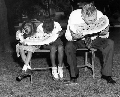 Governor Gregg Cherry eating watermelon with children, 1945-1949. Image from the collections of the North Carolina Museum of History, used courtesy of the North Carolina Department of Cultural Resources. A man, Cherry, and two children eat watermelon. They are hunched over large slices of fruit, seated.