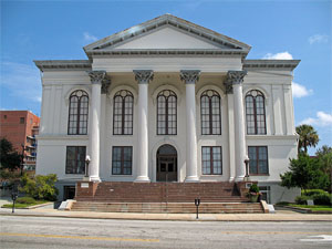 A large classical revival building. It has large columns atop steps. Blue sky in the background.