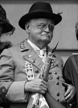 "General" Julian Shakespeare Carr in uniform, November 22, 1923. Image from the Library of Congress. The photograph shows an older man, with glasses and a mustache, wearing military dress and holding a flag. He appears to be with other people who are not in full view in the photo. This photograph of Carr has been excerpted from the original which shows Carr standing with two women and a man.