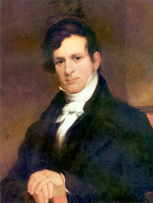 Eaton in a portrait. He has medium hair, and is dressed in finery with a coat and scarf.