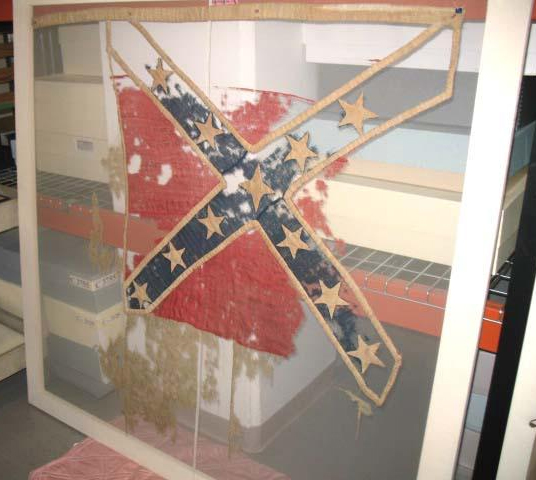 Photograph of surviving fragments of the Confederate Flag of the North Carolina 17th Regiment, reported to have been secretly saved and conveyed to saftey by Thomas Abel and at some ponit into the hands of  Wilson G. Lamb.  The artifact was dispalyed in the North Carolina Hall of History on May 20, 1895 and donated by Lamb to the museum on November 28, 1914.  Item H.1914.2601. from the collections of the North Carolina Museum of History.  Used courtesy of the North Carolina Department of Cultural Resources. 