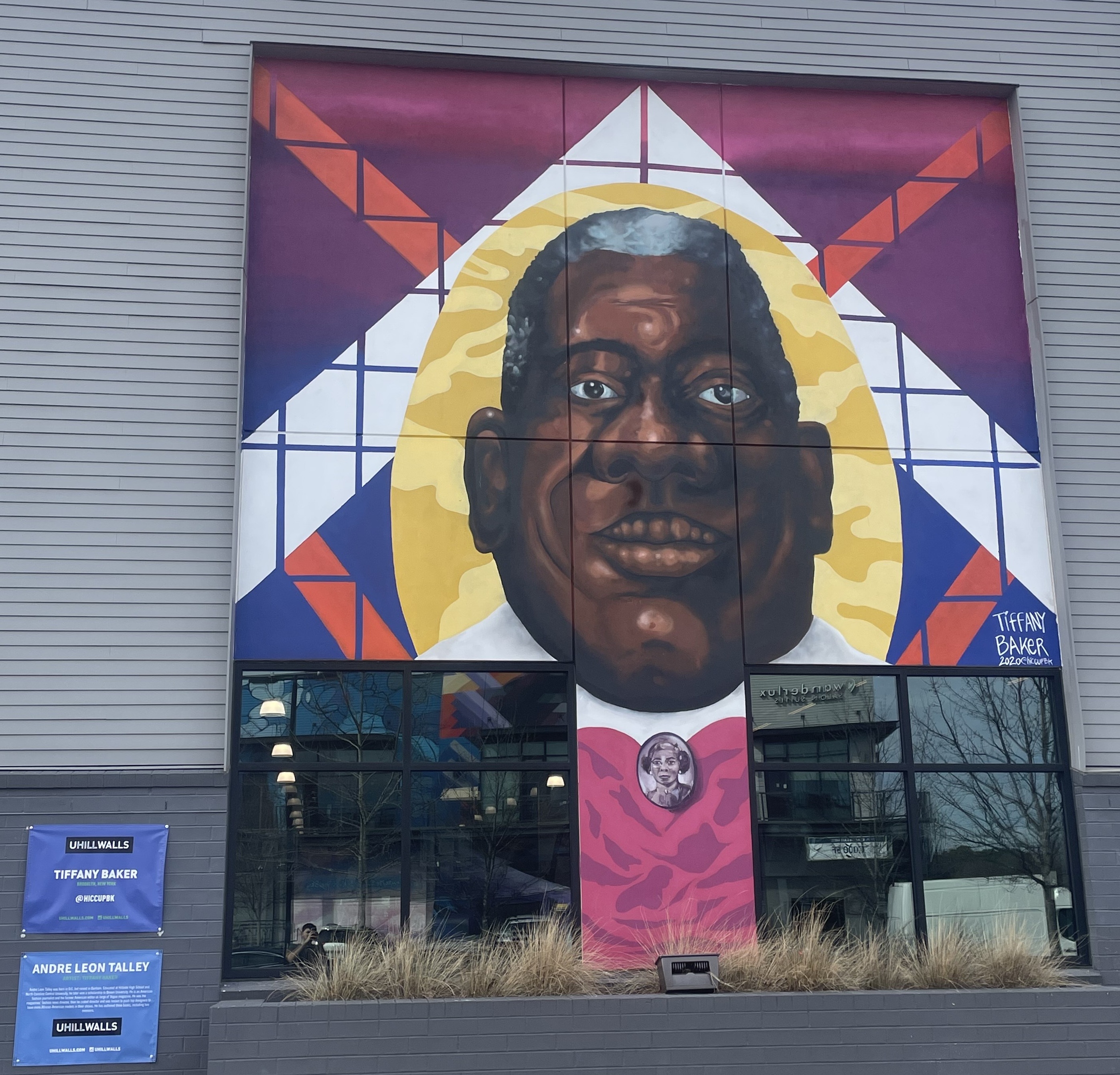 A wall mural depicting Andre Talley. He is smiling with a pink shirt, adorned with a large brooch bearing a woman's visage. He is surrounded by a halo of light.