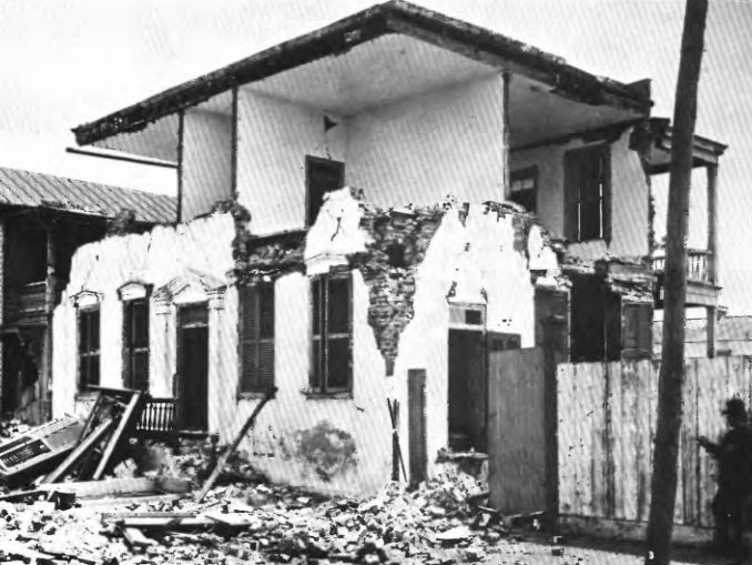 A house in ruins. Rubble lays about. The walls of the second story are destroyed.