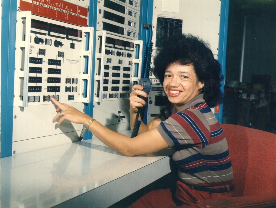 Darden seated in front of a computer switchboard with an audio device in her hand. She is smiling.&nbsp;
