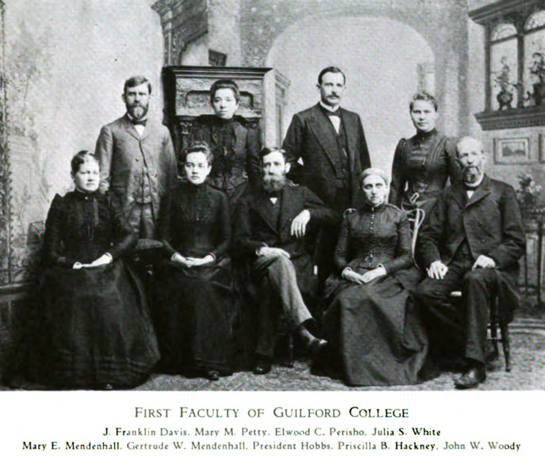 Nine individuals dressed in formal wear seated for a photo. They are wearing dresses, suits, and glasses. John W. Woody is seated farthest right in the photo. 