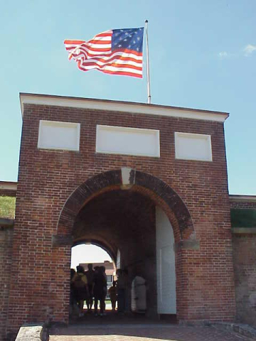 Arched entryway to brick wall of Fort McHenry, an American flag flies overhead